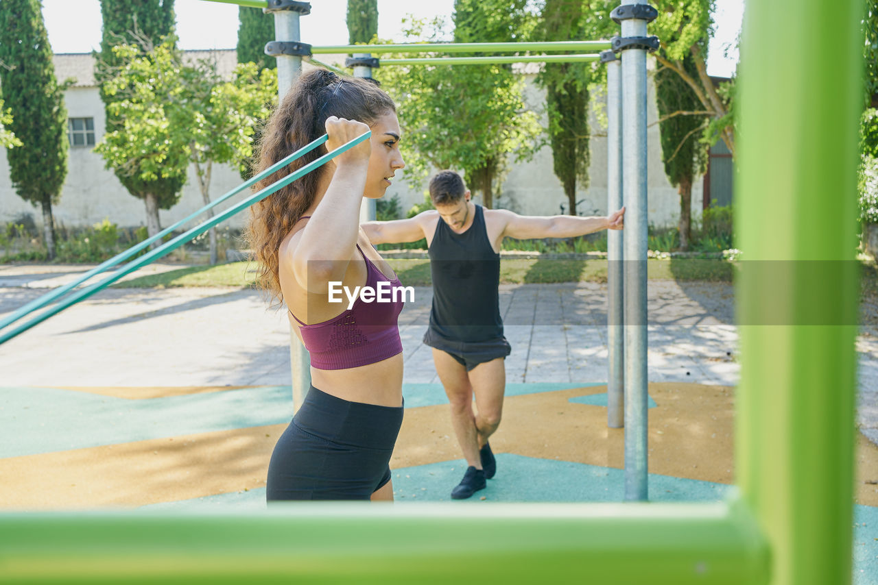 Young woman and man practicing calisthenics in a park on sunny day