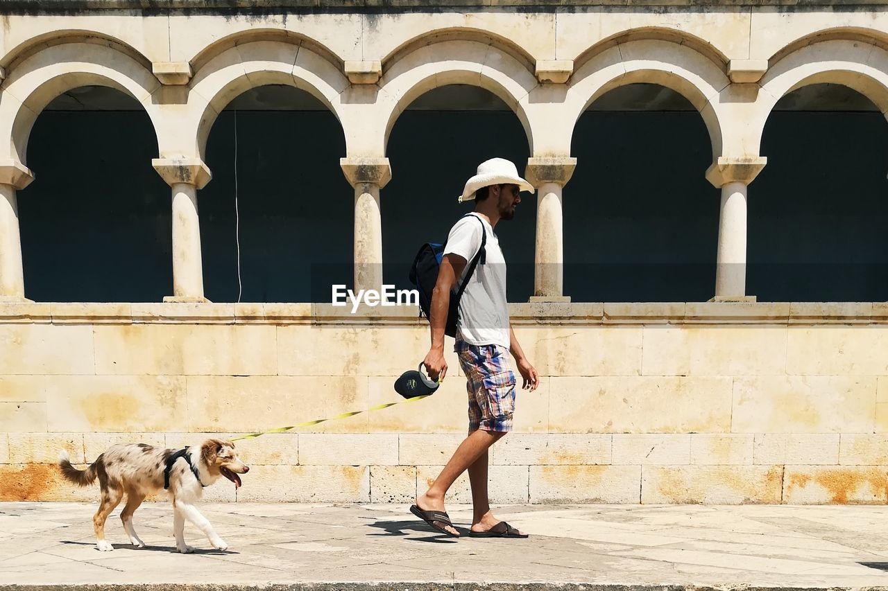 Side view of man with dog walking against built structure