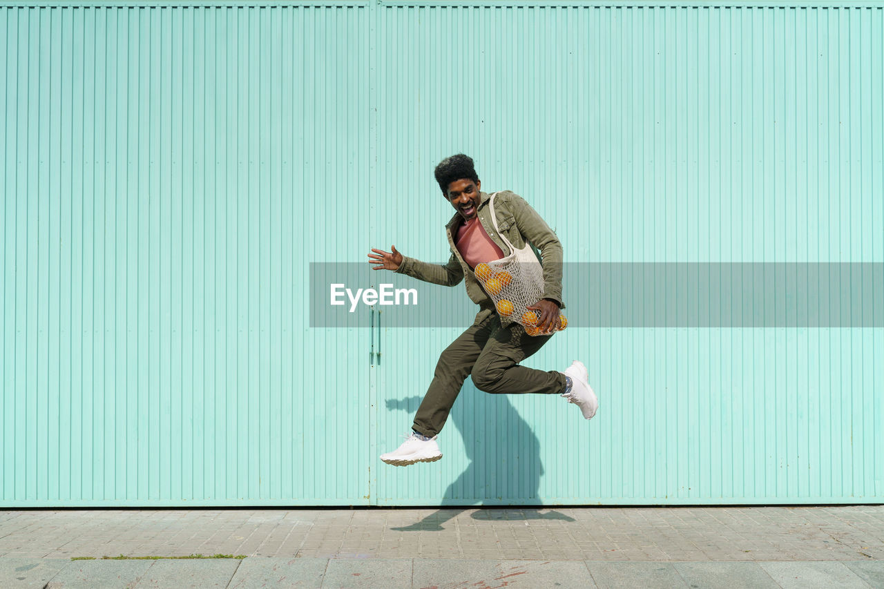 Ecstatic man dancing in front of turquoise wall during sunny day