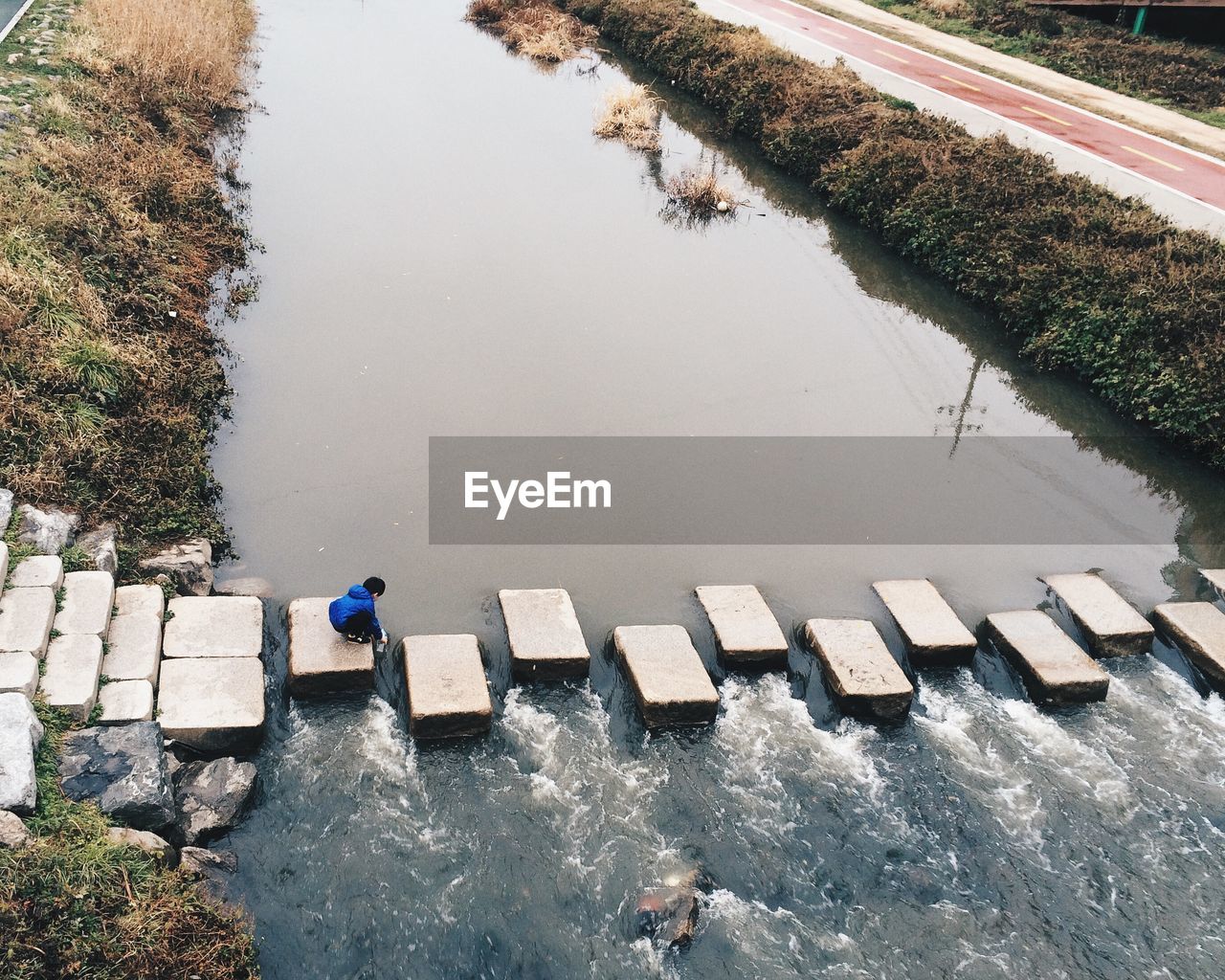 High angle view of boy crouching on stepping stones in river