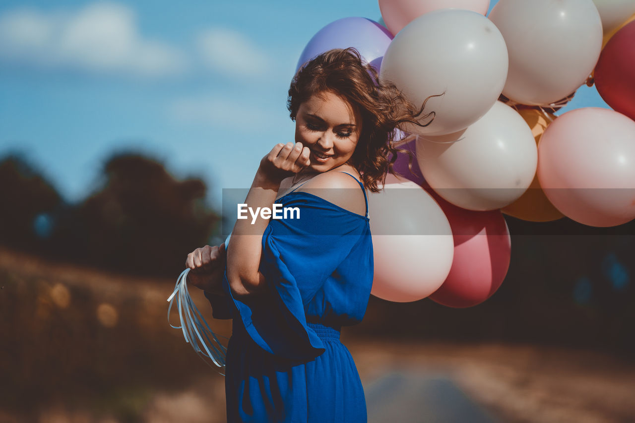 Young woman holding balloons while standing against sky
