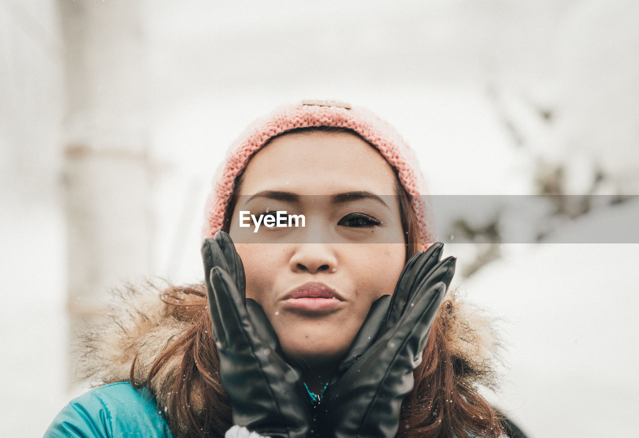 Portrait of woman wearing warm clothing blowing kiss during winter