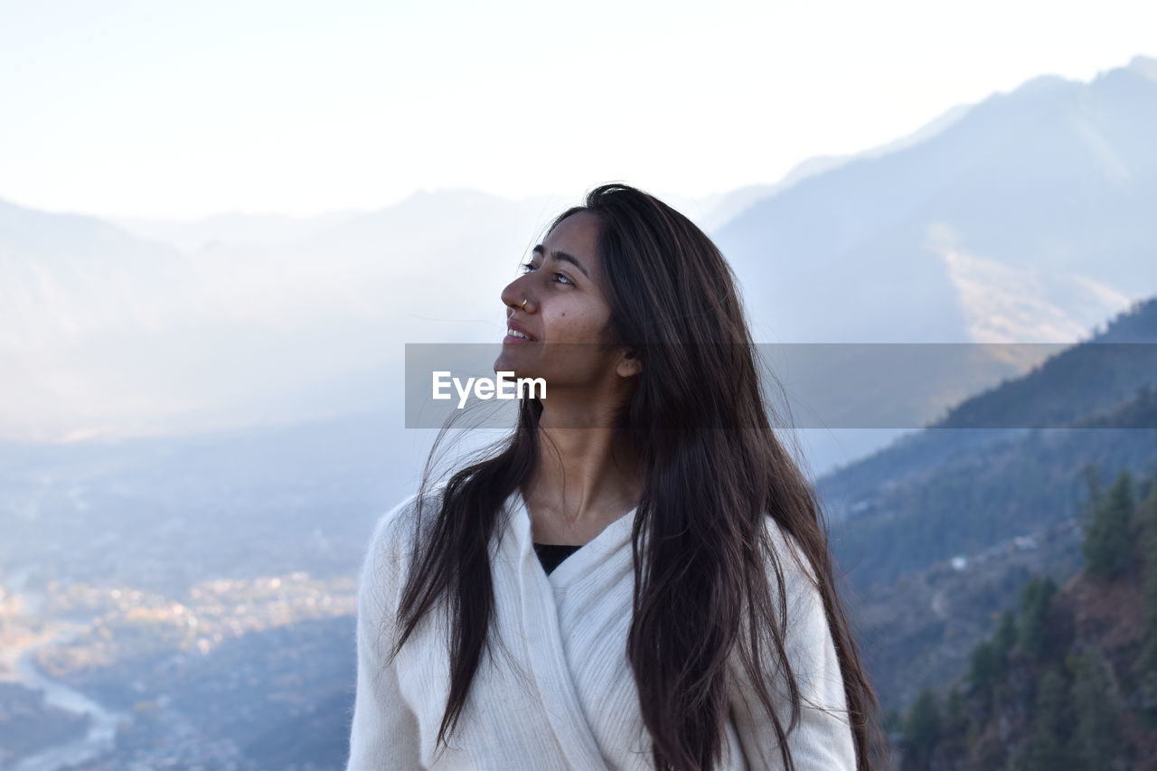 Beautiful young woman looking away against mountains