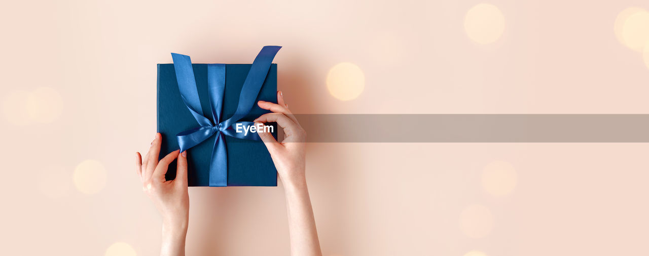 Female hands with festive minimalistic manicure tie a bow on blue gift box. surprise preparation