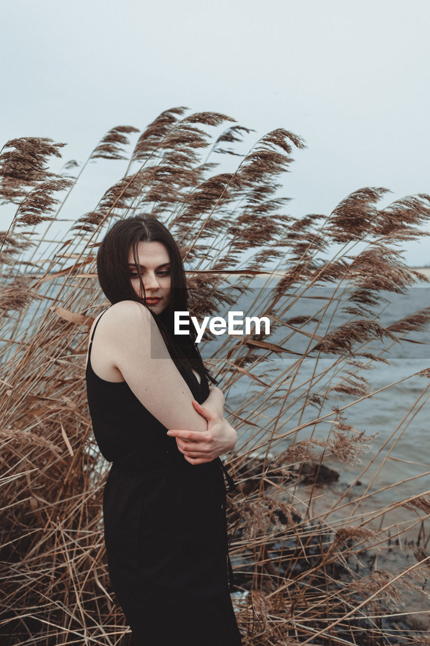 Young woman looking away while standing next to water