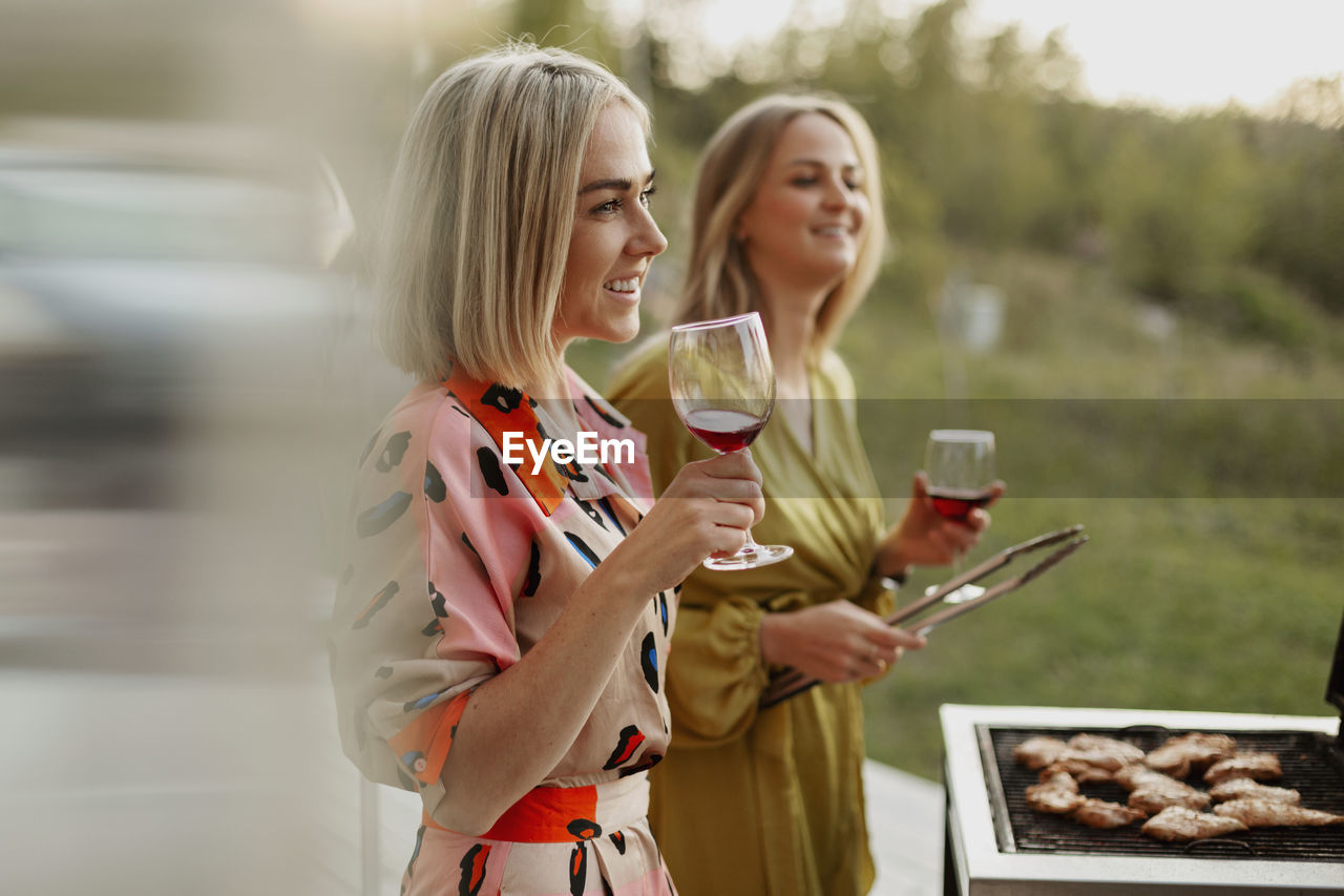 Female friends holding wine glasses and barbecuing meat