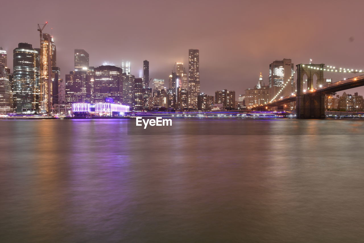 Illuminated city by river against sky at night