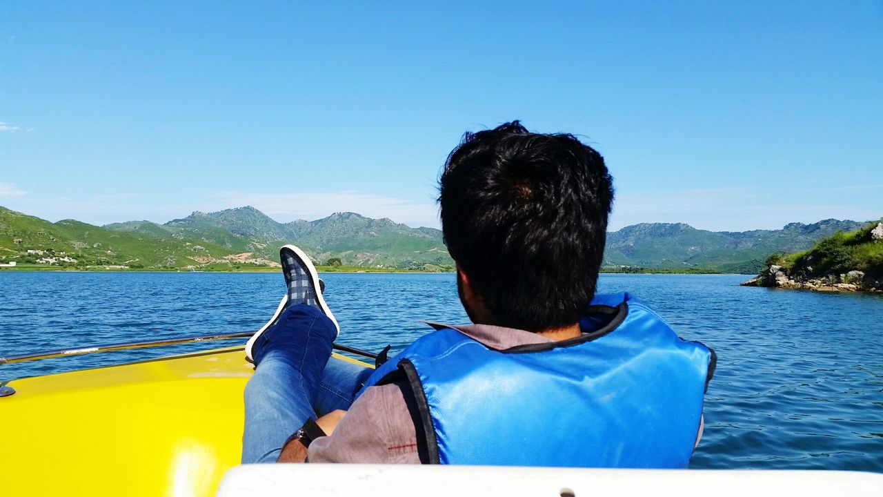 REAR VIEW OF MAN IN BOAT ON LAKE AGAINST SKY
