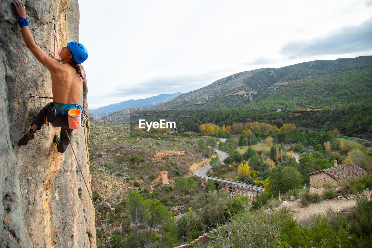 Shirtless man rock climbing against sky