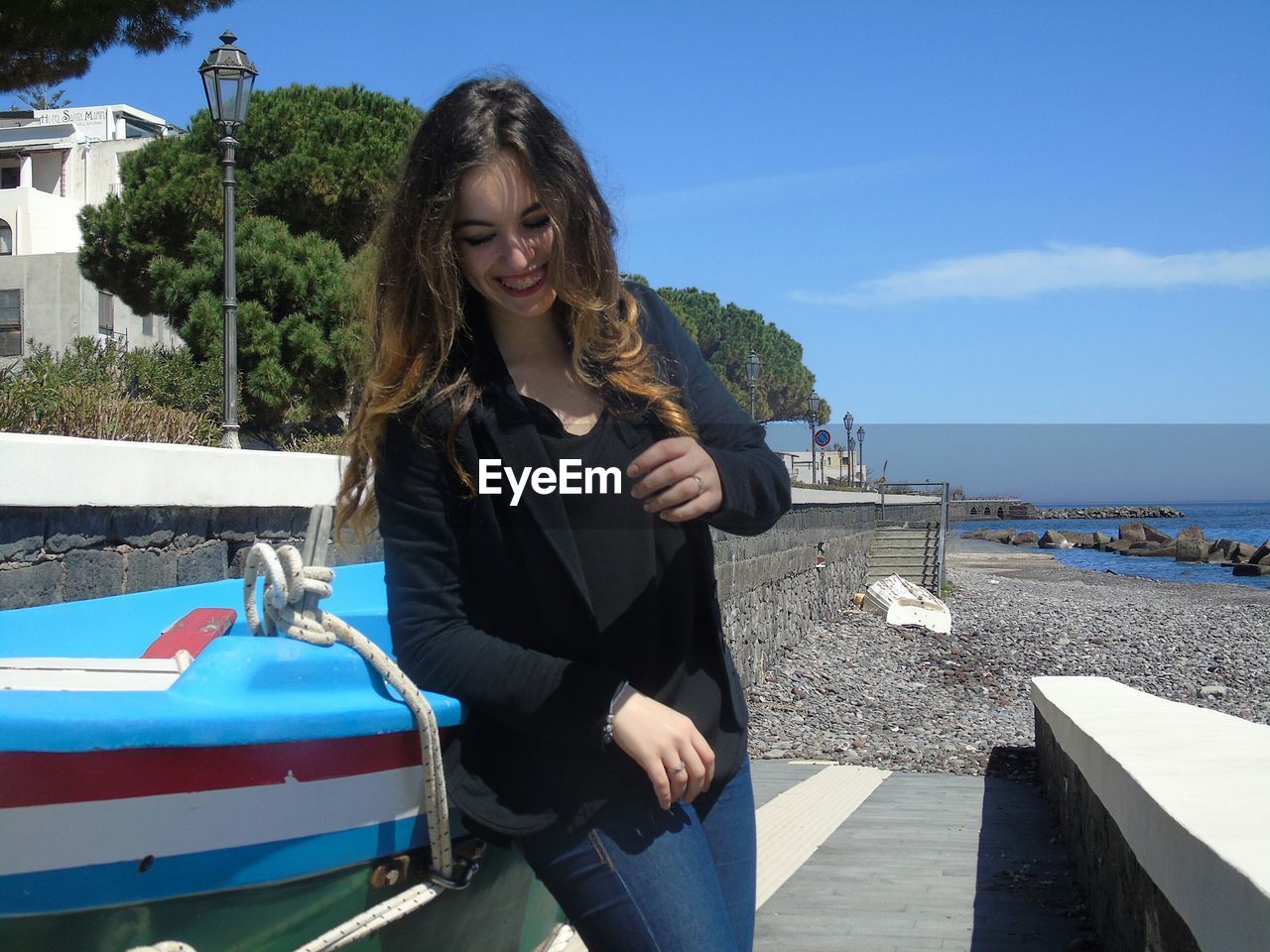 Beautiful woman laughing by boats at beach against sky