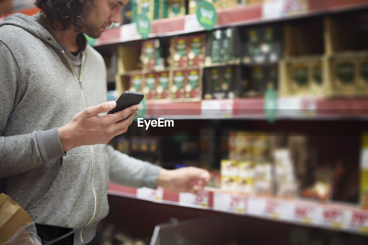 Man in supermarket comparing prices during inflation on cell phone