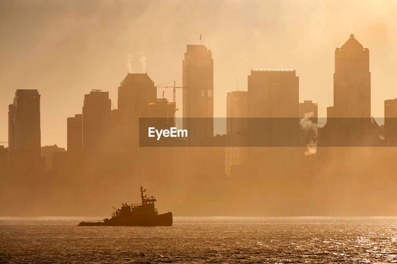 Tug boat on elliott bay against buildings in city during foggy weather