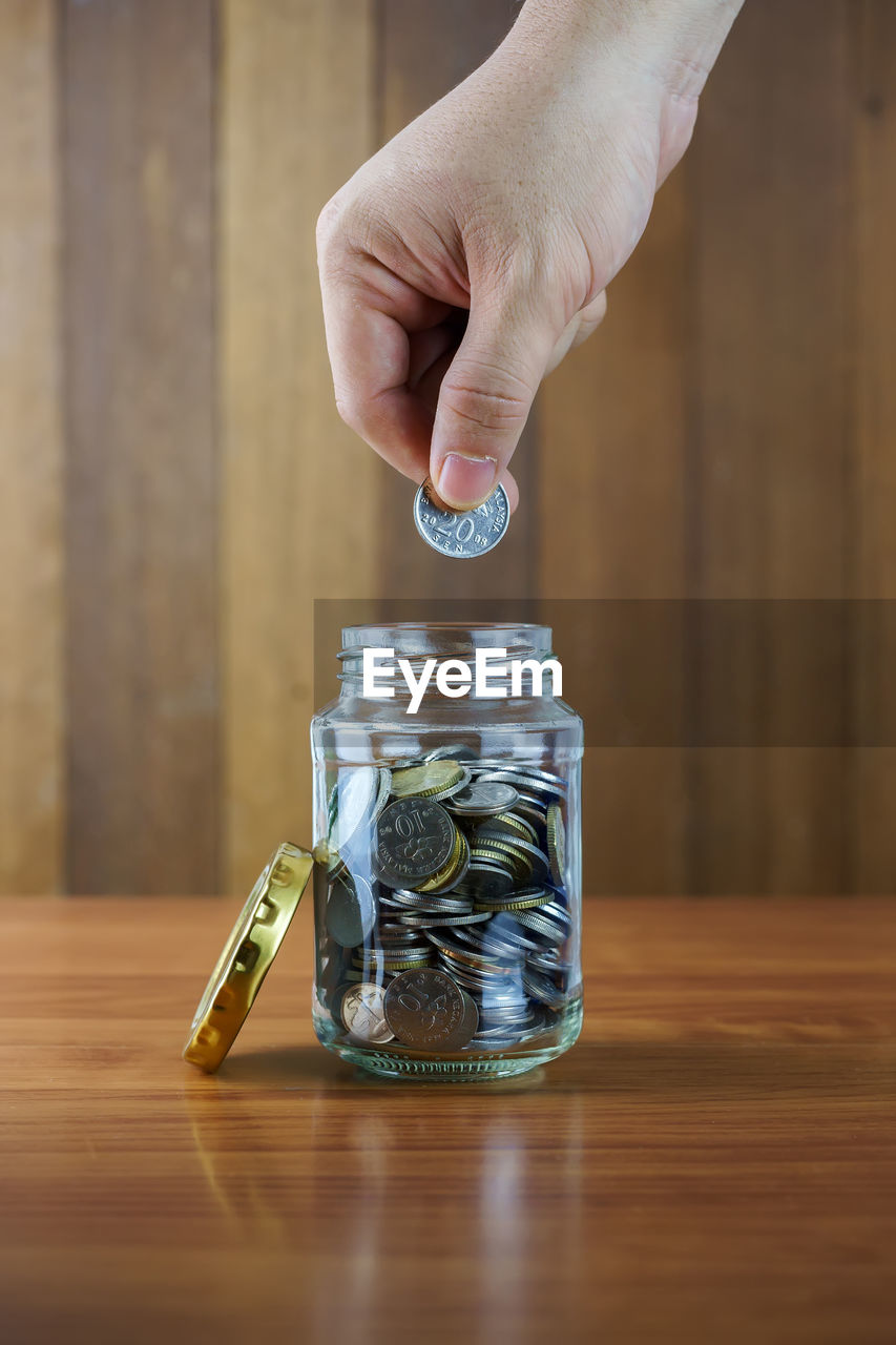 Close-up of hand putting coin in jar on table