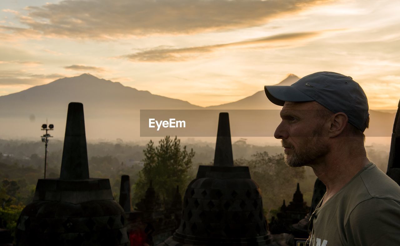 Profile view of man with historic temples in background against sky