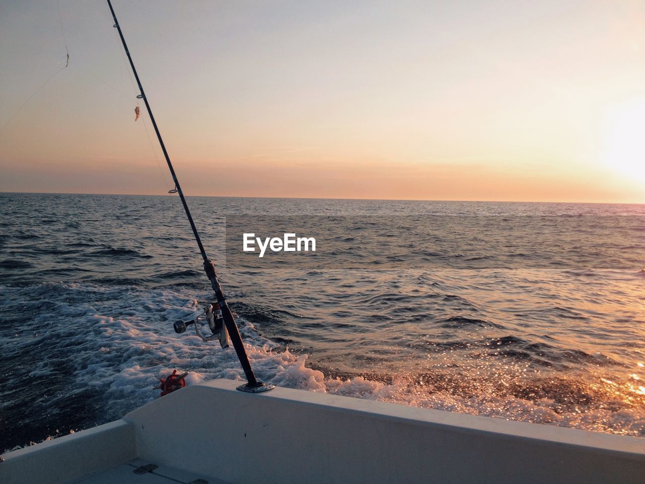 Fishing rod on nautical vessel at sea against sky during sunset