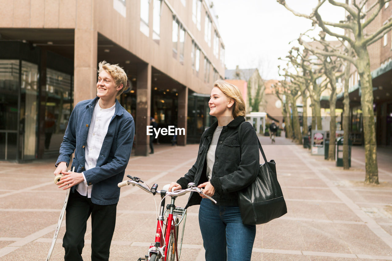 Smiling young couple traveling with skateboard and bicycle in city