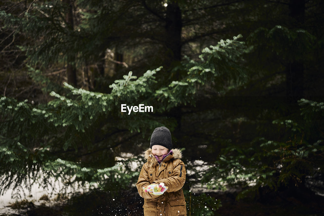 Happy child making snowball near fir tree in forest