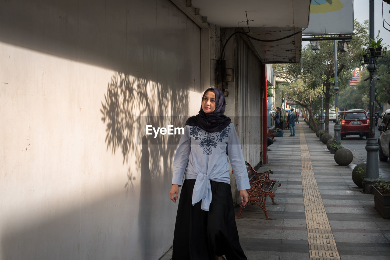 Smiling woman walking on footpath against building