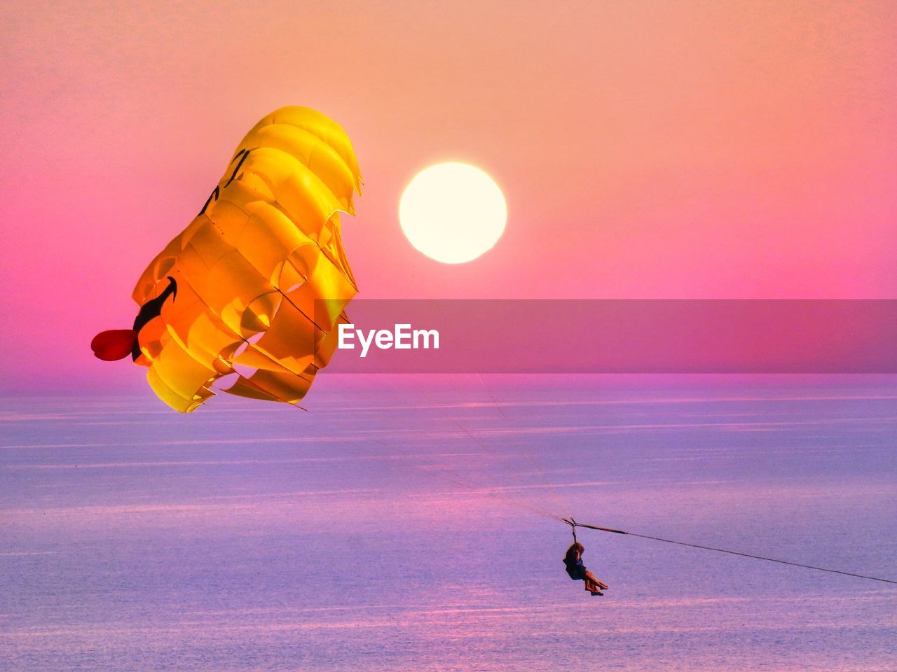sunset, sky, nature, parachute, flying, orange color, water, mid-air, beauty in nature, sea, motion, sports, adventure, transportation, one person, scenics - nature, sun, environment, outdoors, balloon, silhouette, land, horizon, extreme sports, tranquility, holiday, travel, landscape, yellow, dusk, leisure activity