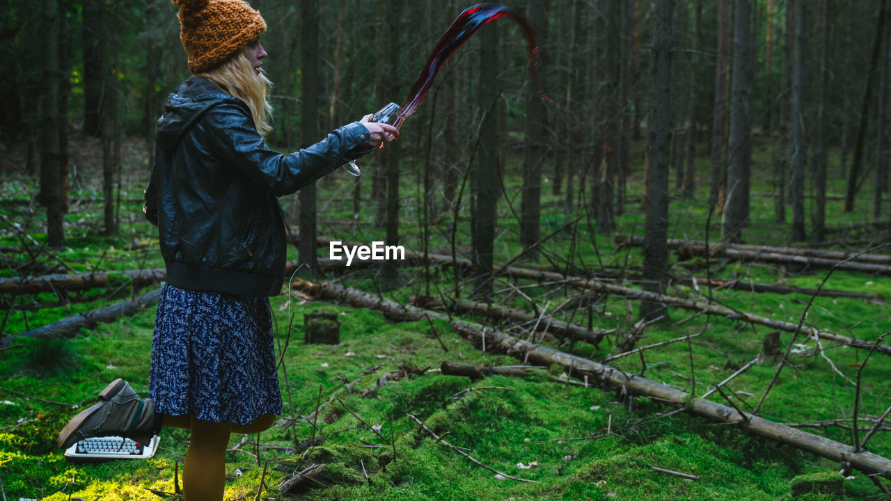 Girl in skirt and hat spilling red wine in mossy forest