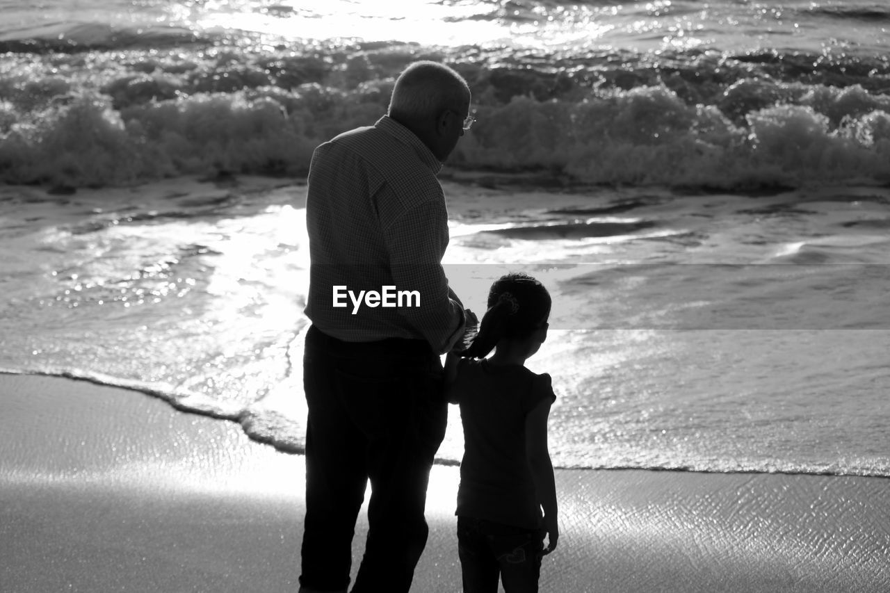 High angle view of grandfather standing with granddaughter at beach