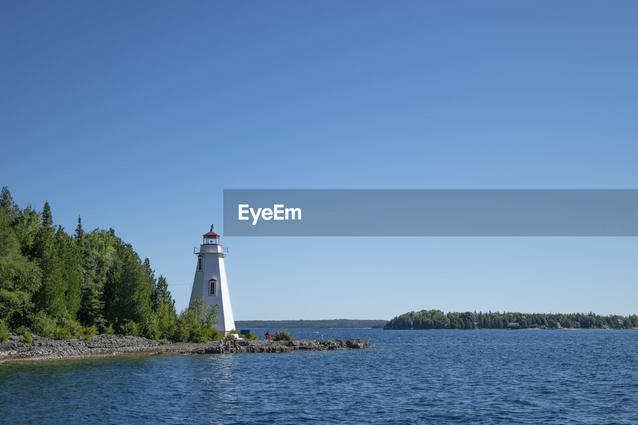 lighthouse, water, guidance, architecture, sky, built structure, tower, building, building exterior, blue, sea, clear sky, nature, security, protection, travel, travel destinations, plant, scenics - nature, day, copy space, land, no people, tree, beach, bay, outdoors, landscape, coastline, transportation, sunny, tranquility, nautical vessel, environment, beauty in nature, non-urban scene, cloud, tranquil scene, tourism, summer, coast, shore, sunlight