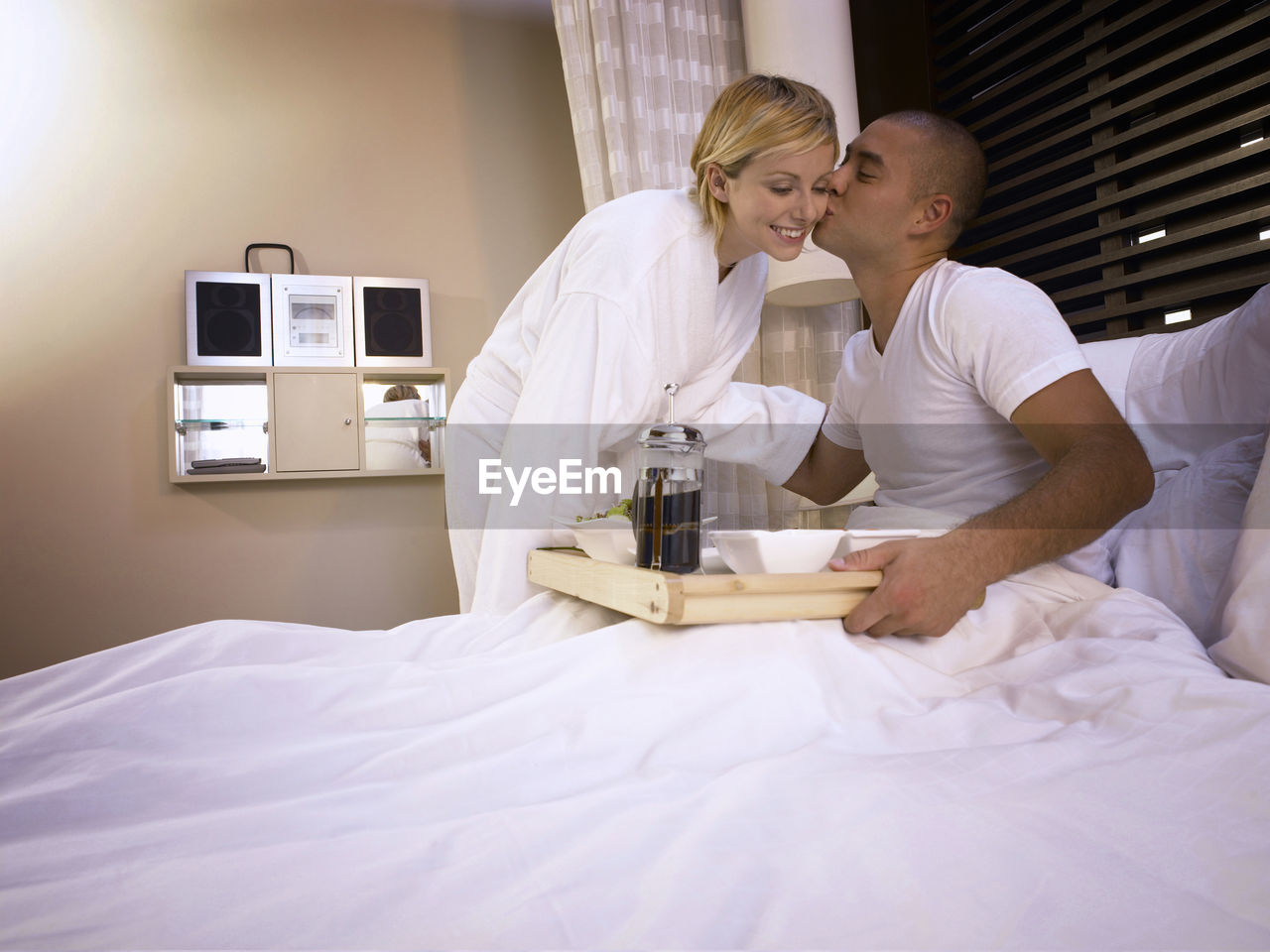 Man kissing girlfriend on bed in hotel room