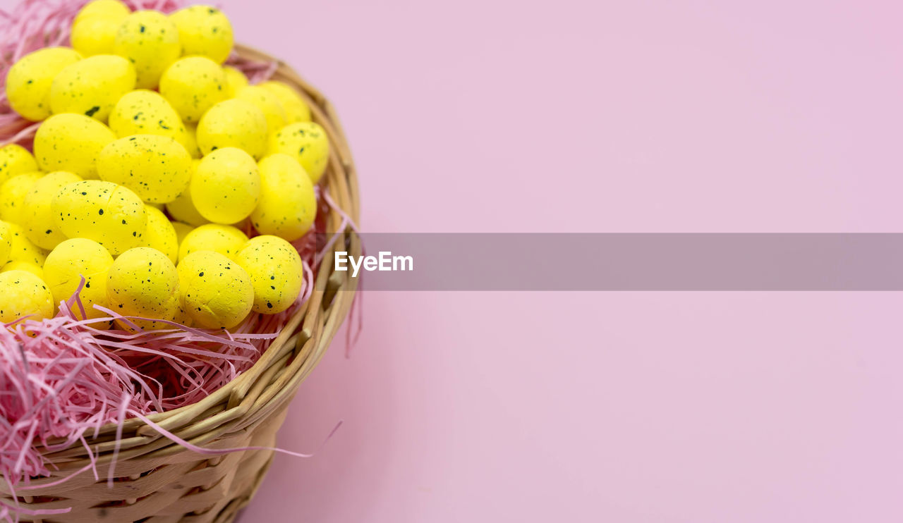 Yellow easter egg with freckles pattern inside a basket on pink background. closed up multi colored