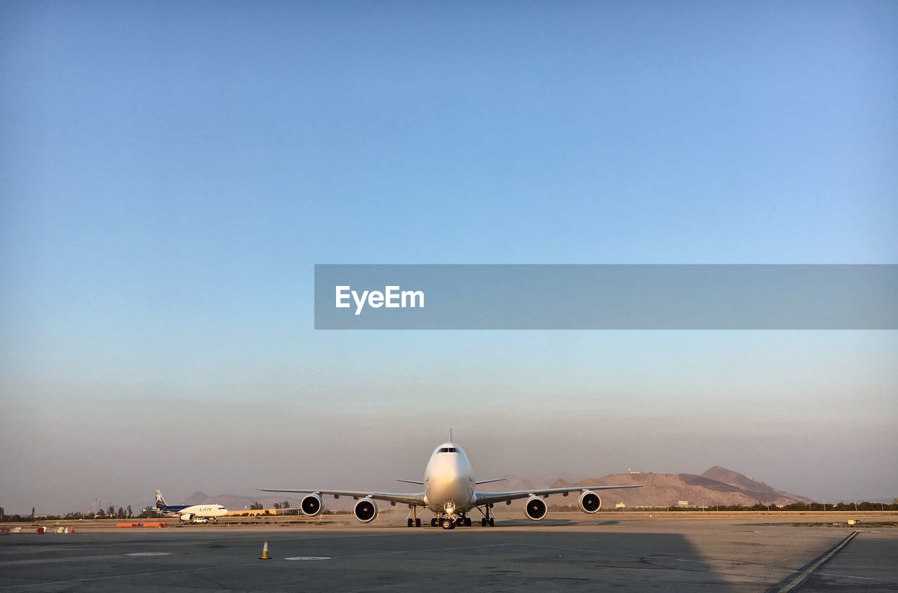 Airplane on airport runway against blue sky during sunset