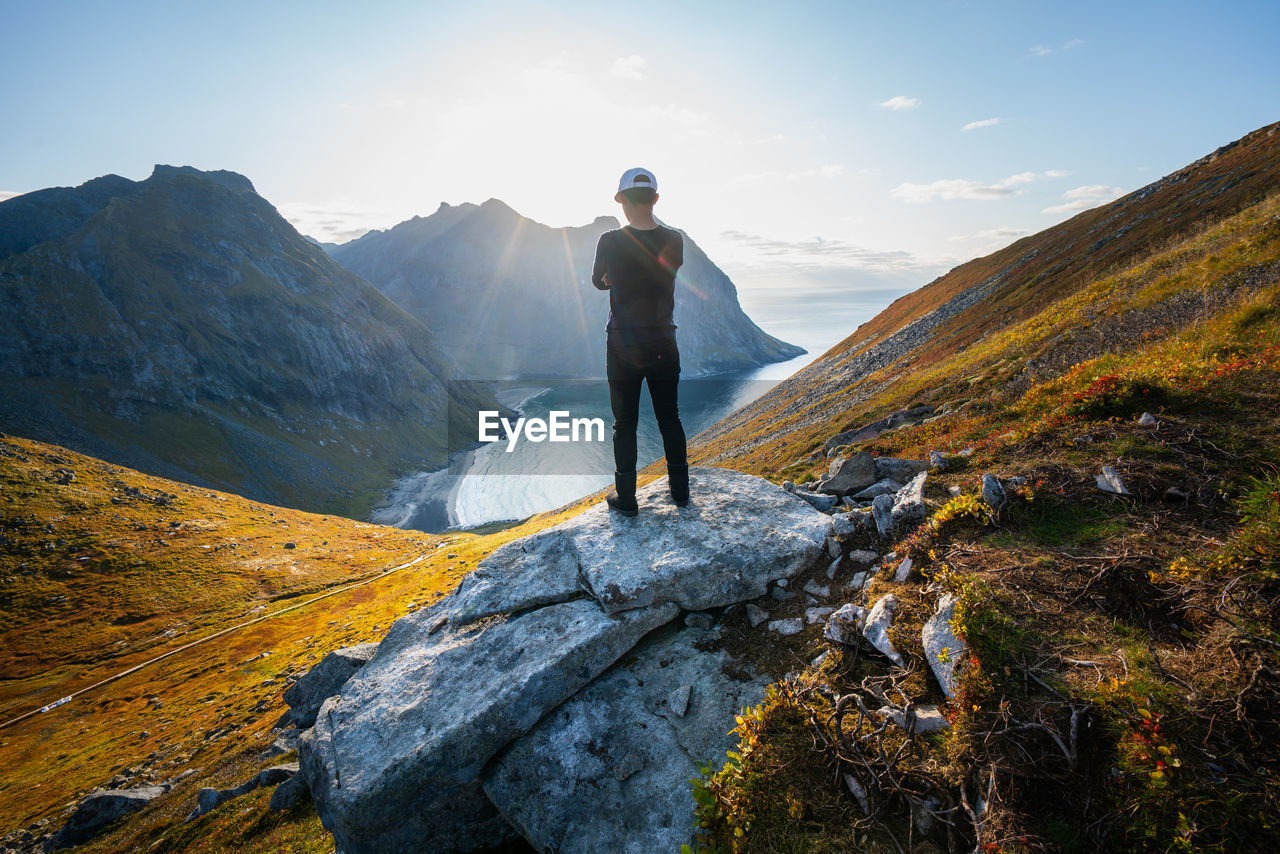 Rear view of man standing on rock against sky