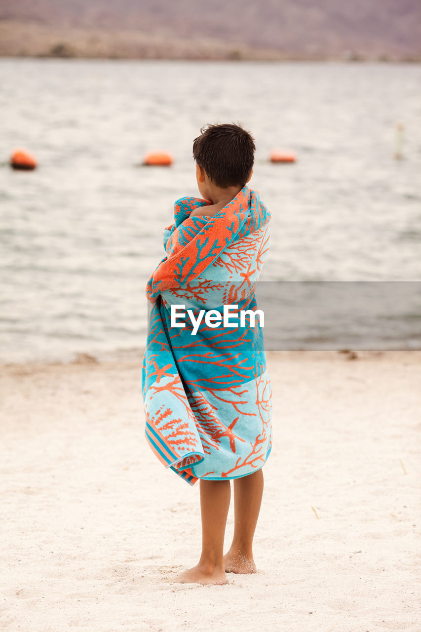 Boy wrapped in towel while standing at beach