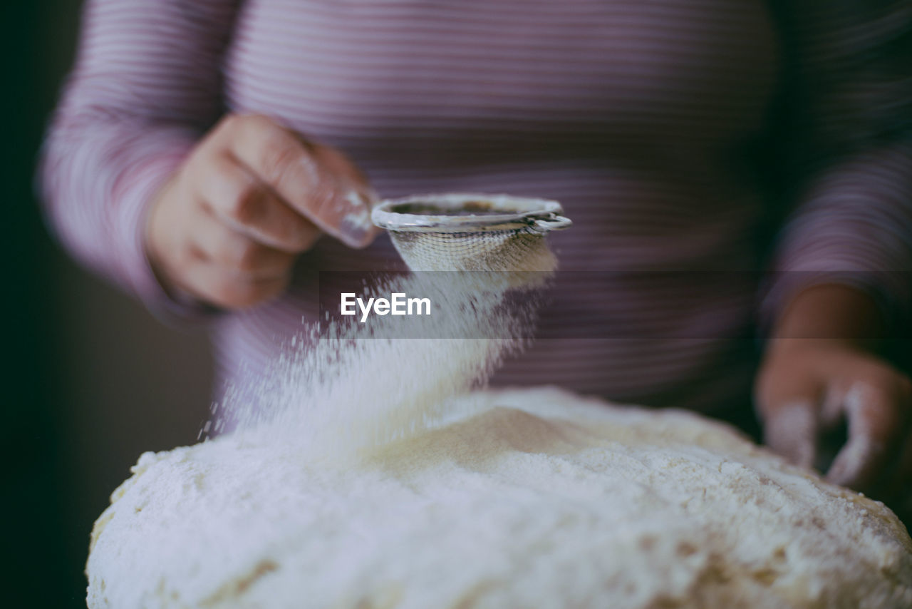 Midsection of woman sieving flour in kitchen