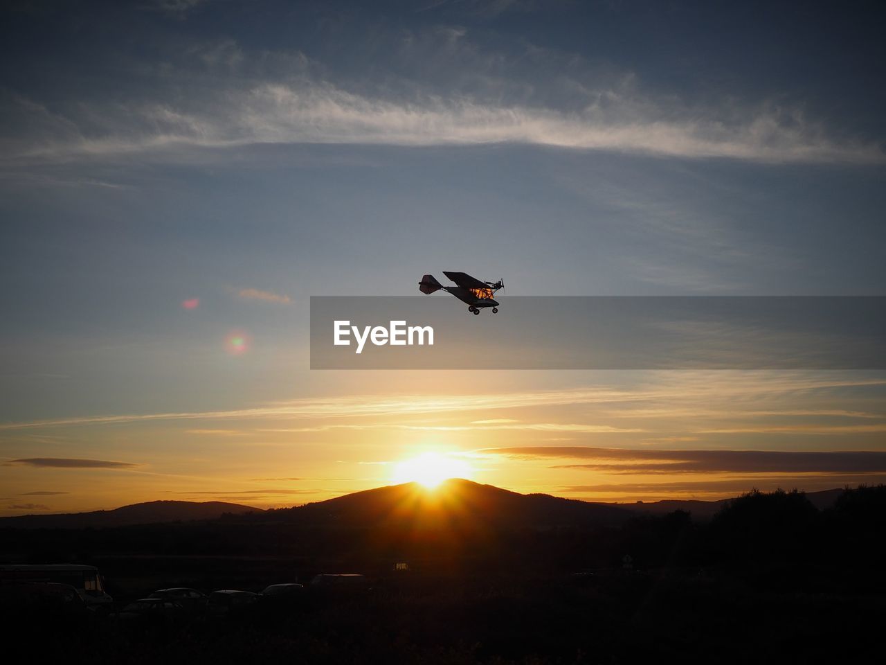 Low angle view of light aircraft flying over silhouette mountains during sunset