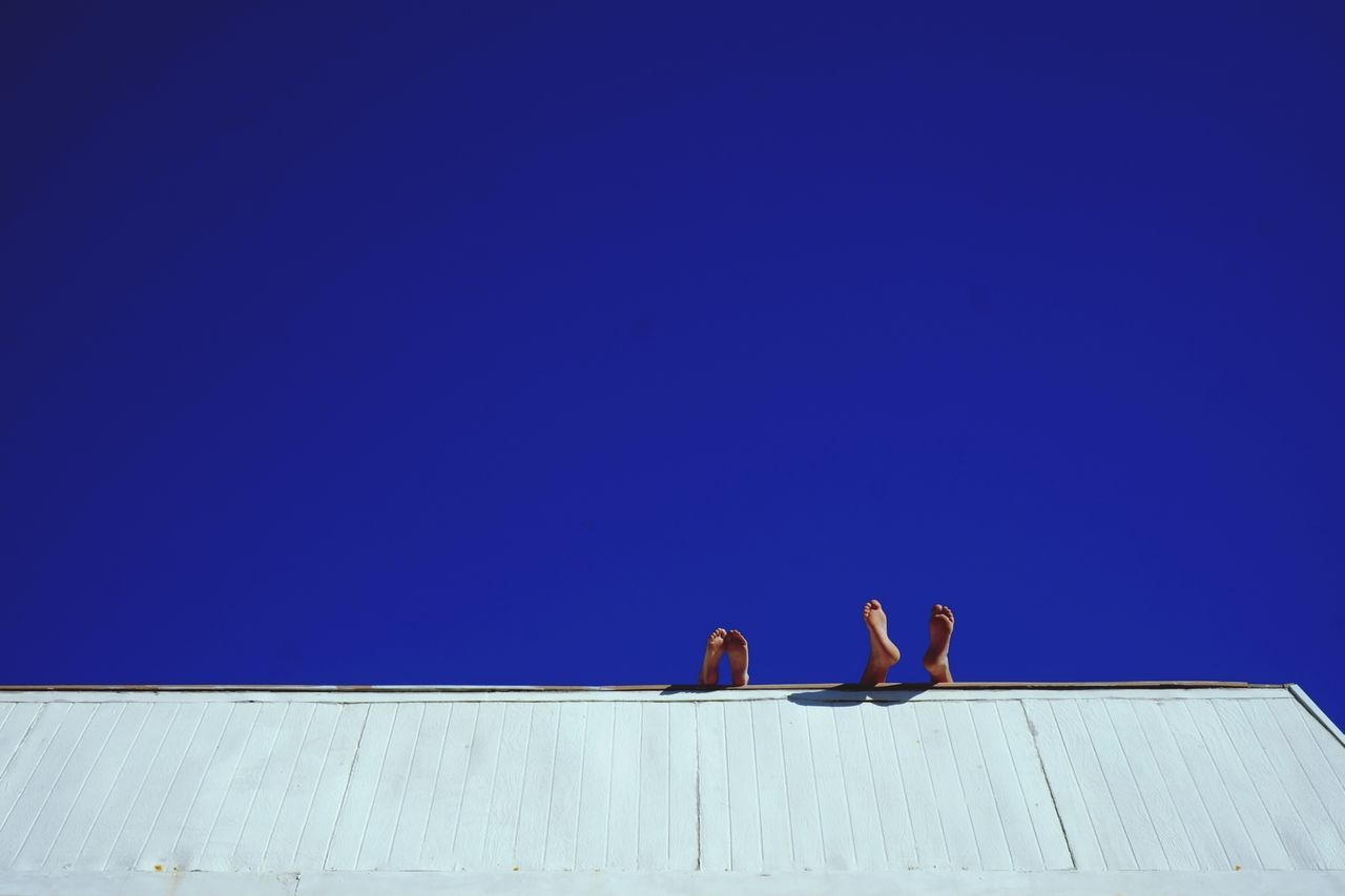 Bare feet on building edge against blue sky