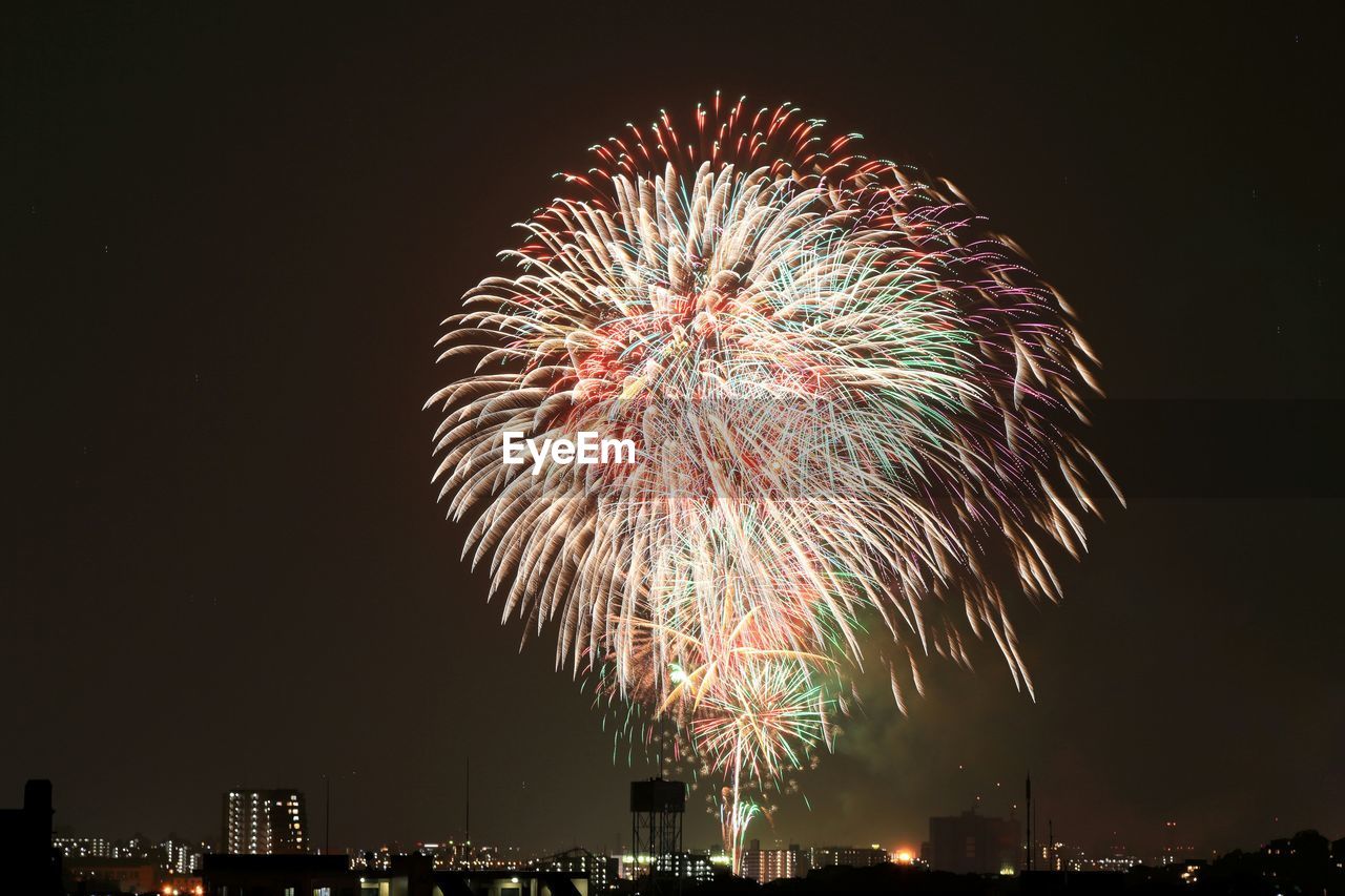 Low angle view of colorful firework exploding over illuminated city