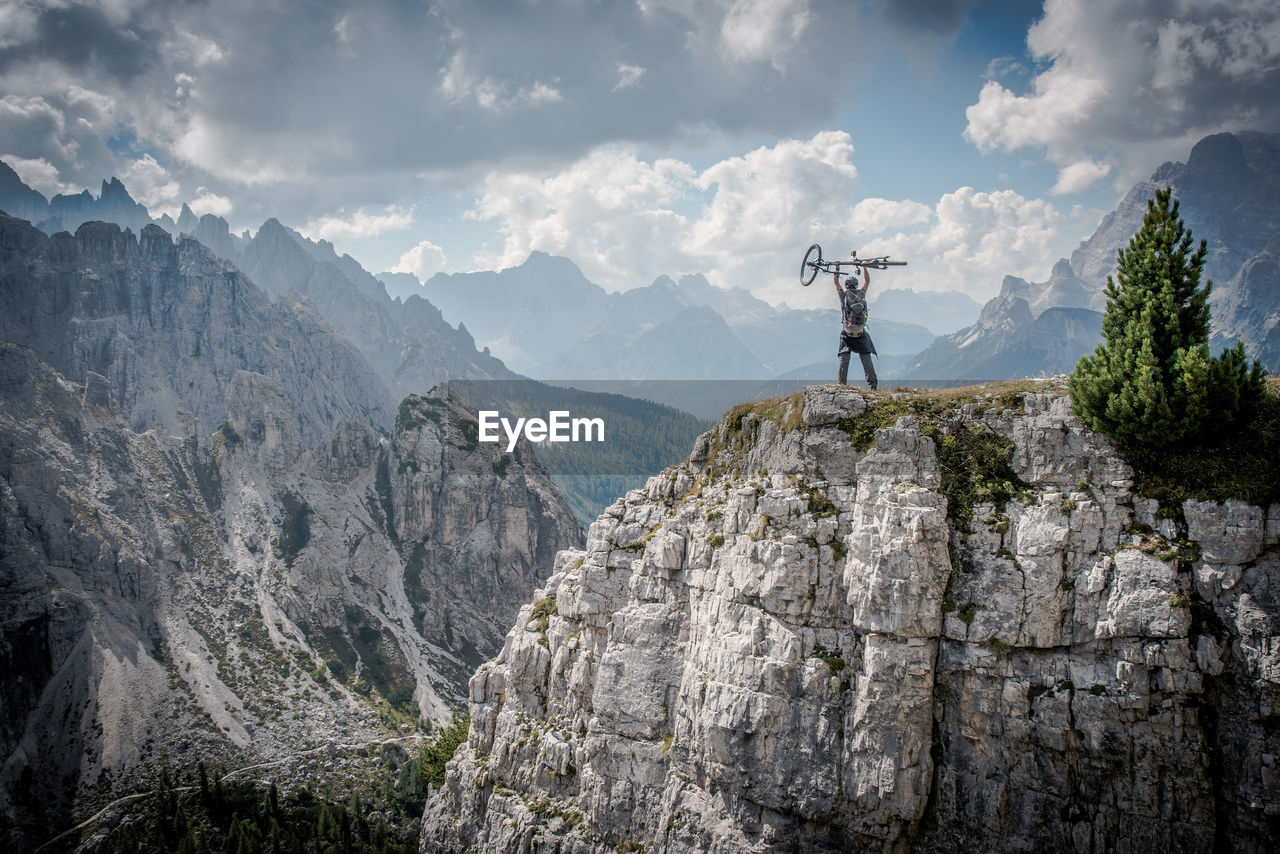 Man standing on cliff against cloudy sky