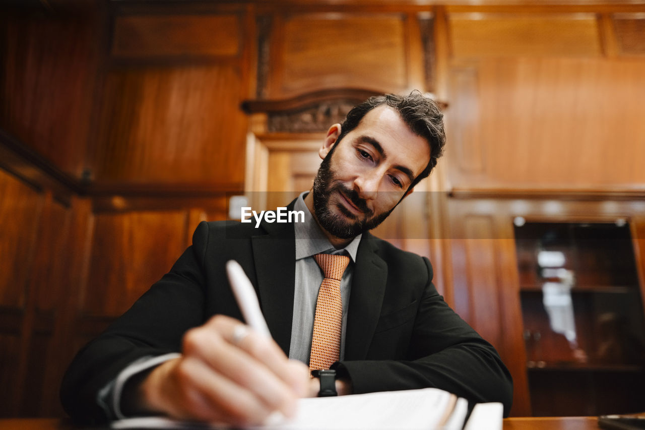 Confident bearded male lawyer signing contract document in board room during meeting