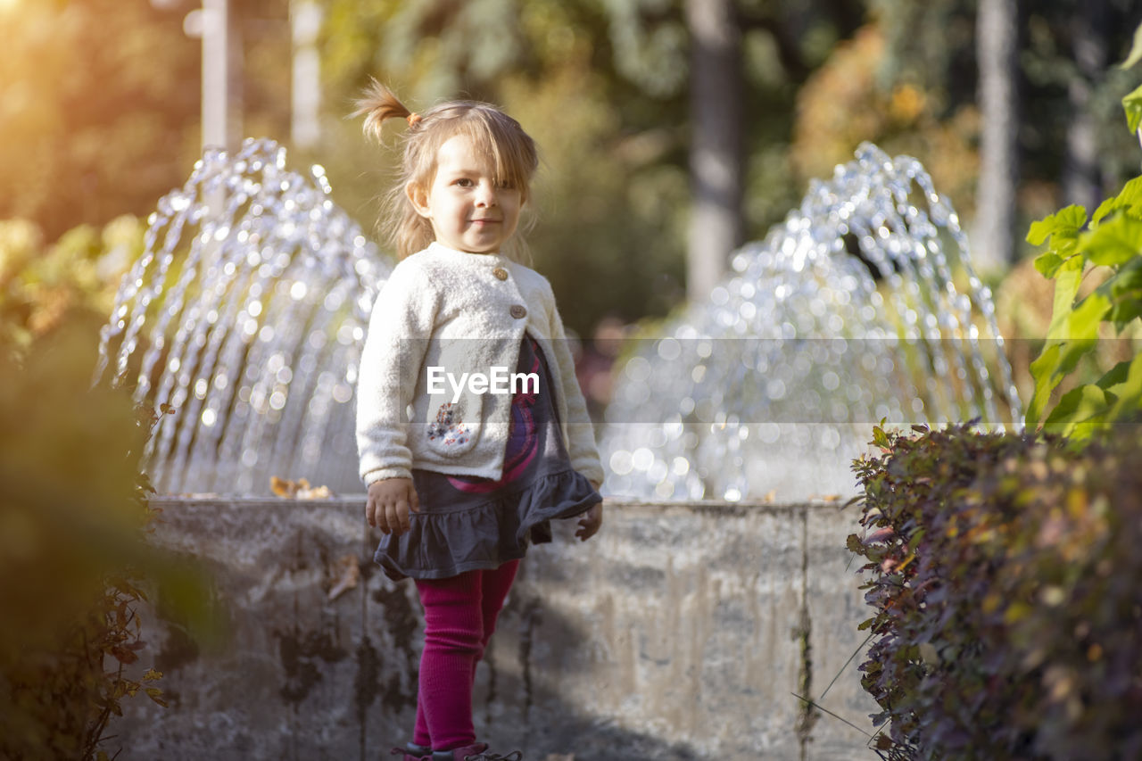 Charming toddler in the park with fountains in the background