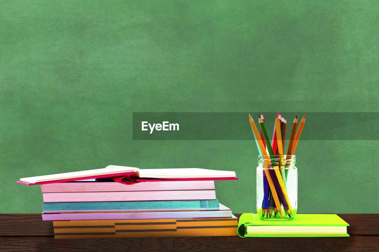 Close-up of multi colored pencils and books on table against green wall