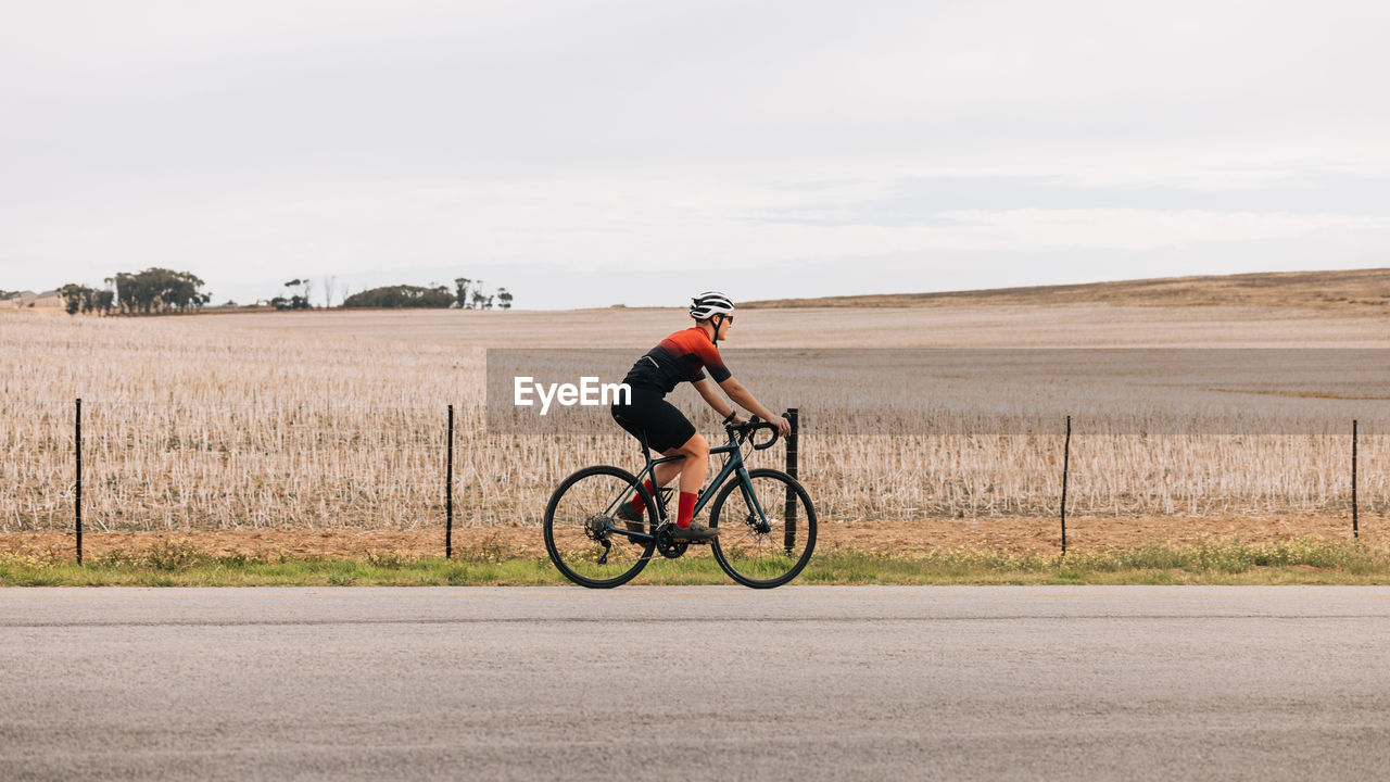 rear view of man riding bicycle on field against sky