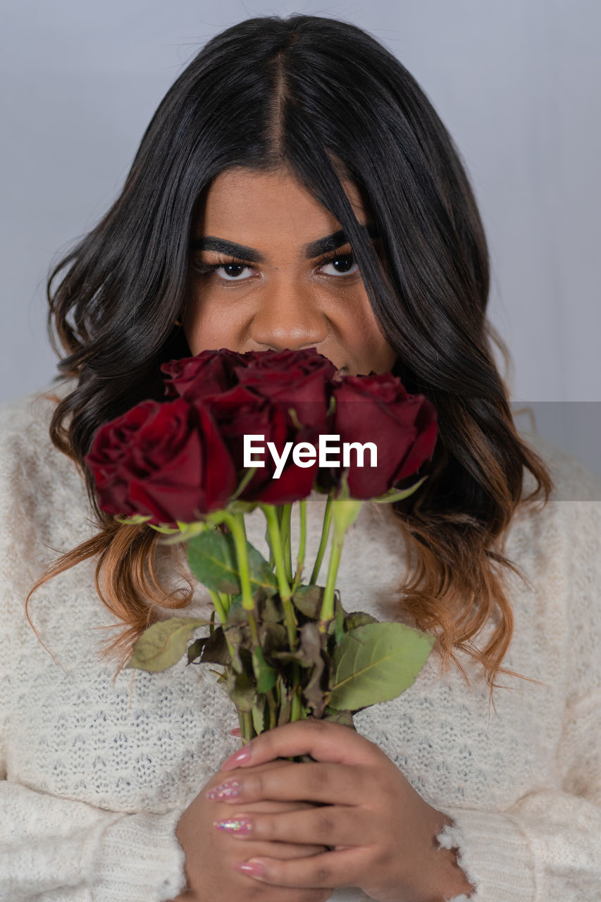 PORTRAIT OF WOMAN HOLDING ROSE BOUQUET AGAINST WALL