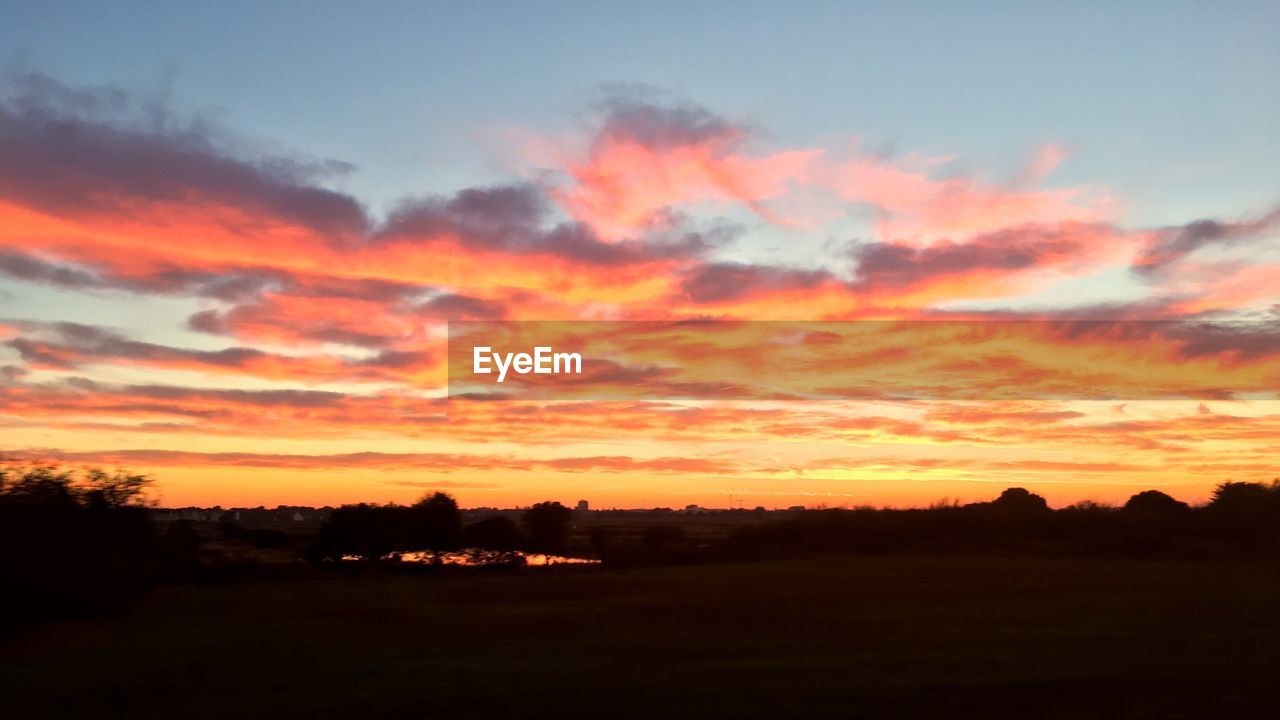 SCENIC VIEW OF SILHOUETTE FIELD AGAINST SKY AT SUNSET