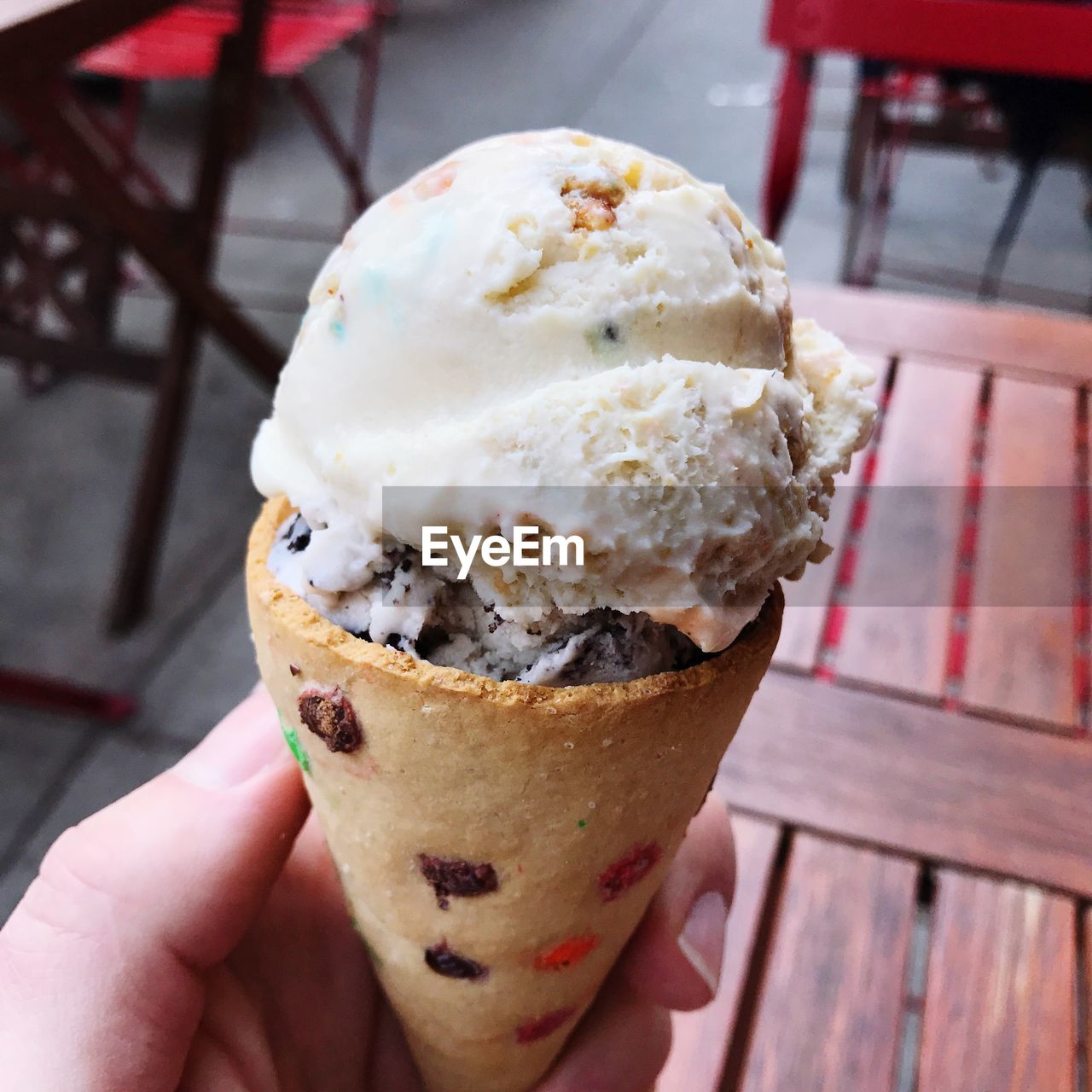 CLOSE-UP OF HAND HOLDING ICE CREAM CONE ON TABLE