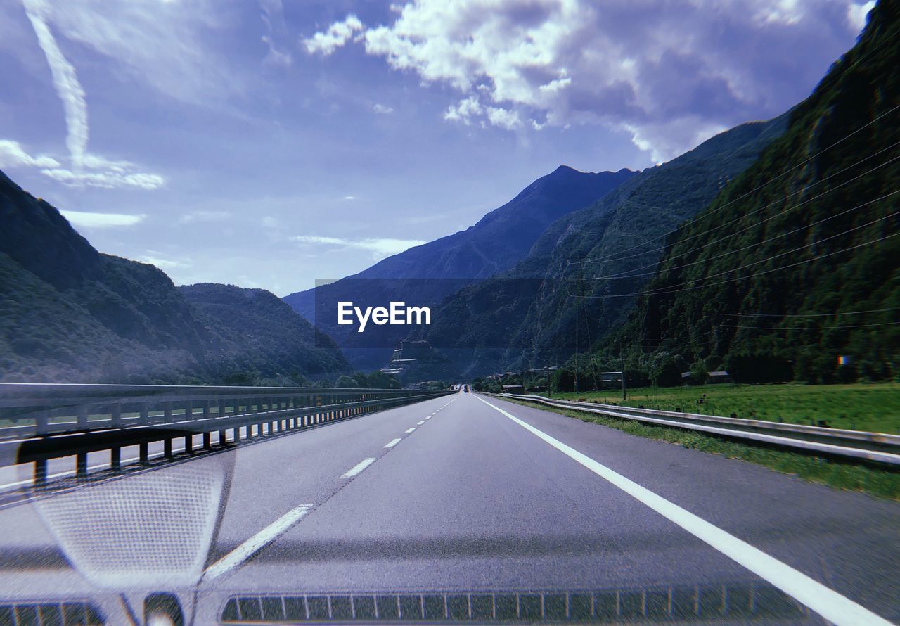 Empty road leading to mountains seen through car windshield against sky