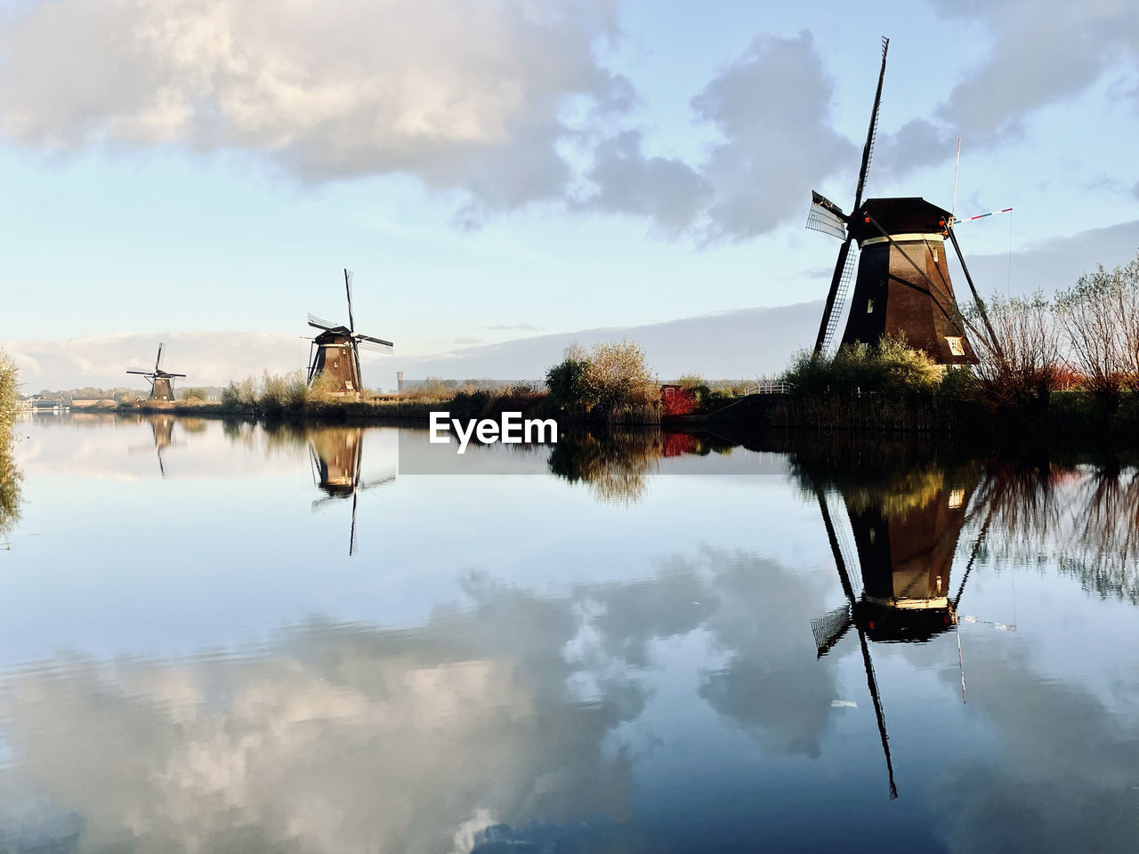windmill, water, reflection, wind turbine, wind power, turbine, sky, environmental conservation, renewable energy, environment, alternative energy, nature, lake, mill, cloud, traditional windmill, power generation, rural scene, landscape, morning, beauty in nature, architecture, tranquility, no people, machine, outdoors, day, social issues, built structure, scenics - nature, vehicle, nautical vessel