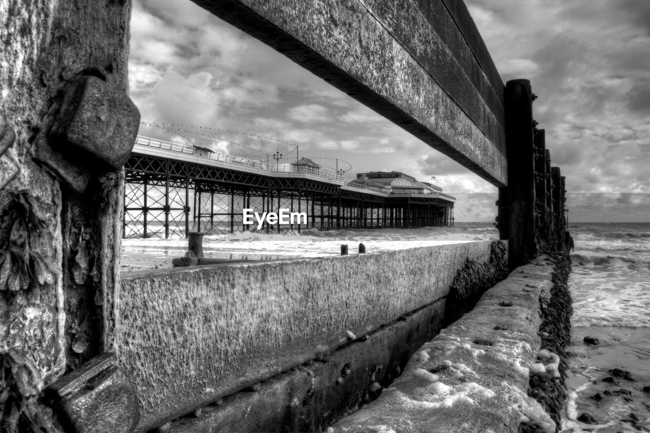 Cromer pier in sea against sky seen from weathered wooden post