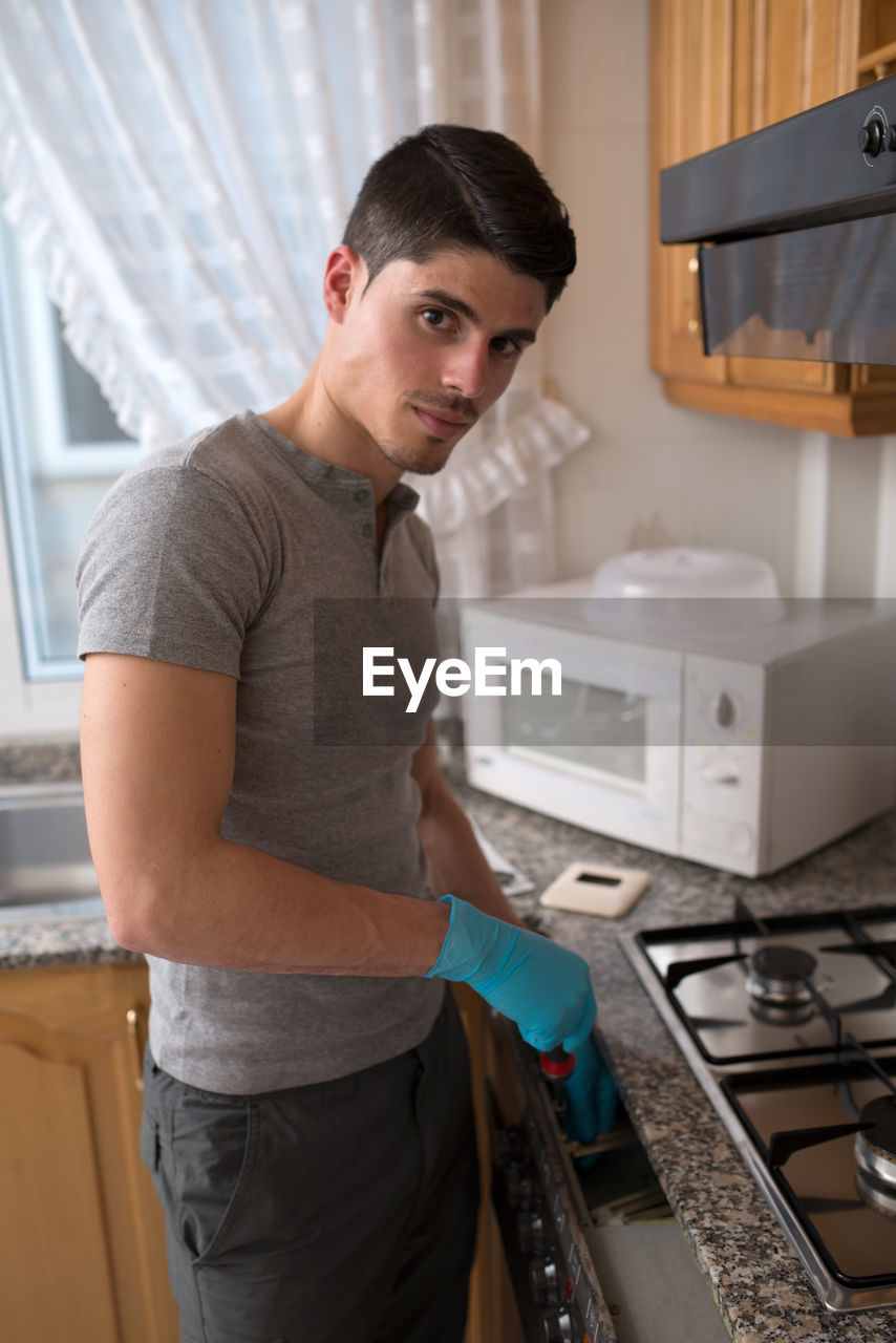 Portrait of young man repairing stove in kitchen