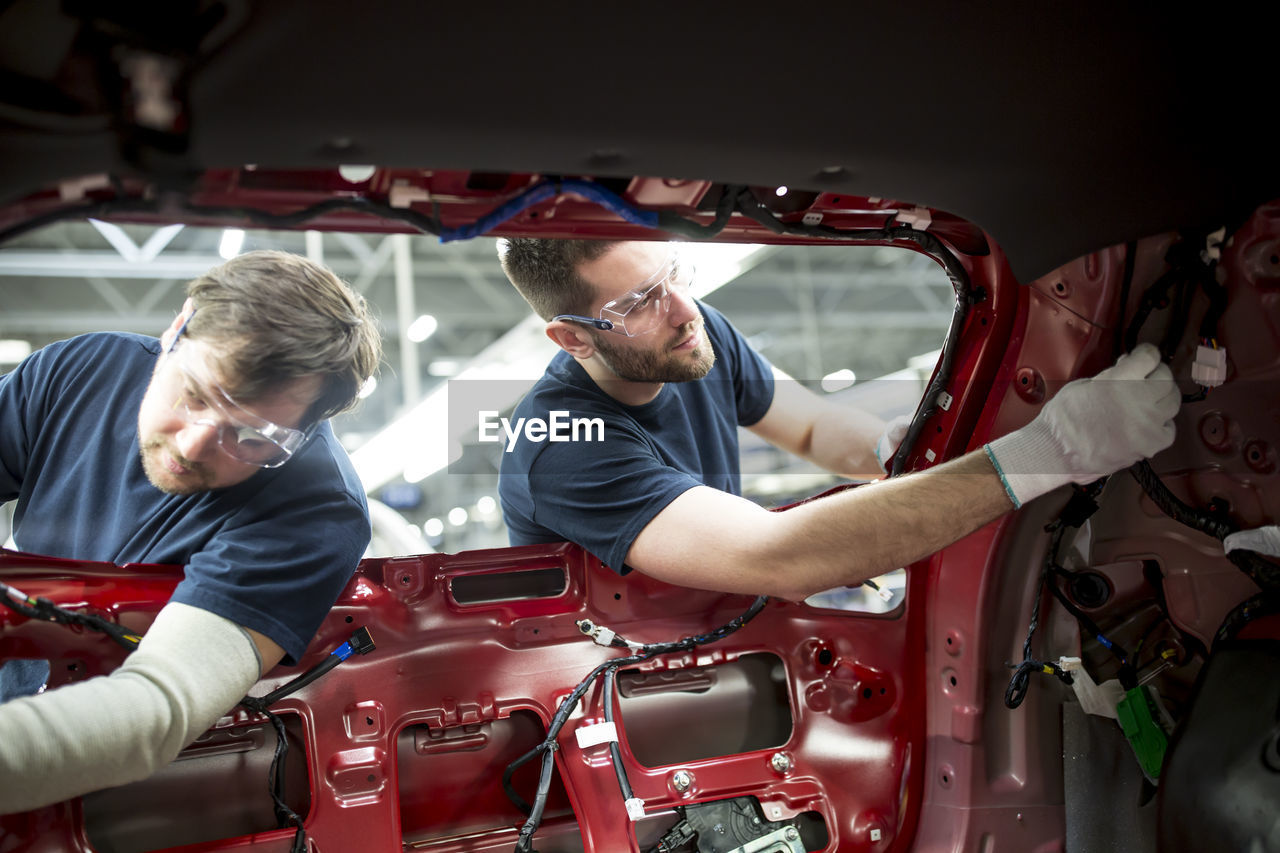 Two colleagues working at bodywork in modern car factory