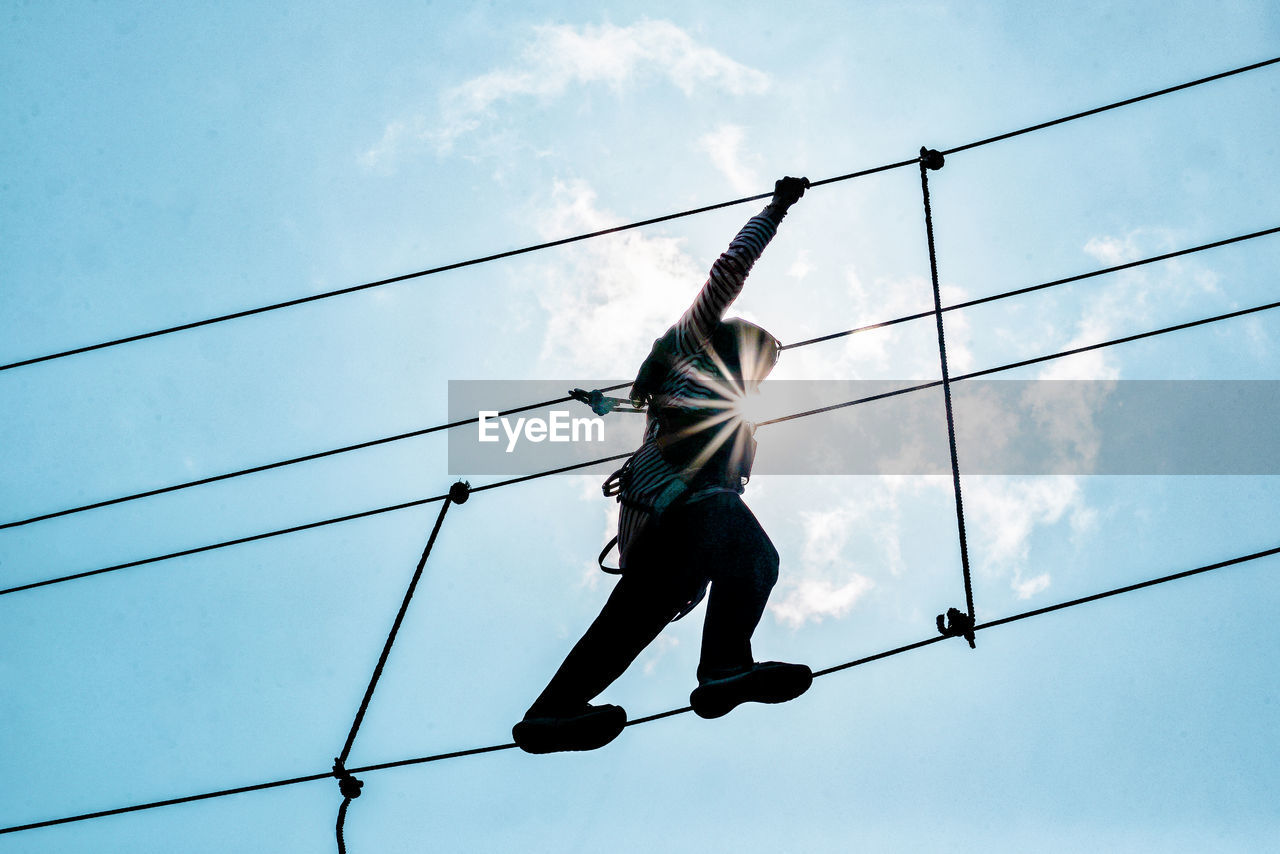 Low angle view of woman walking on tightrope against sky