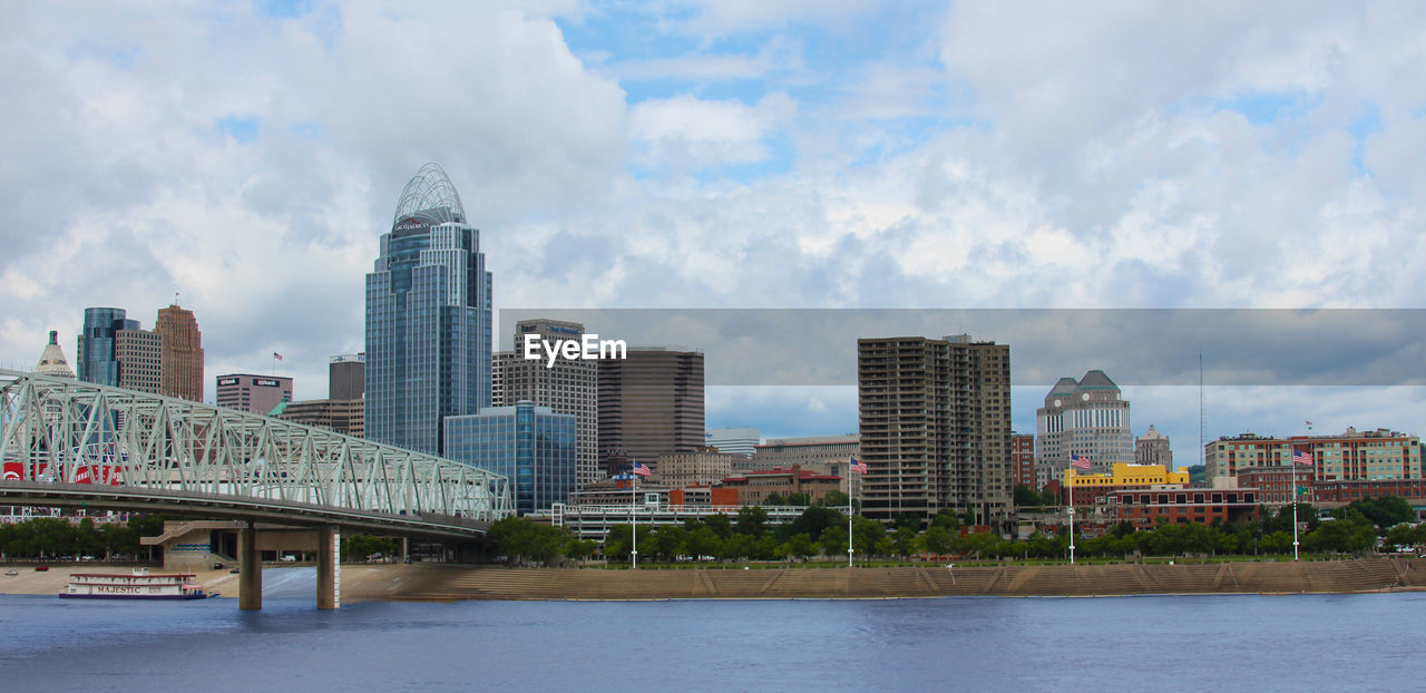 Modern buildings by river against sky in city